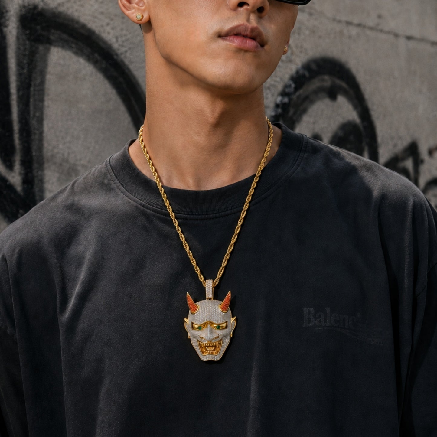 Male model wearing the ICEDIAMOND 18k gold finish LET LIGHT IN Oni mask pendant necklace with a streetwear outfit.
